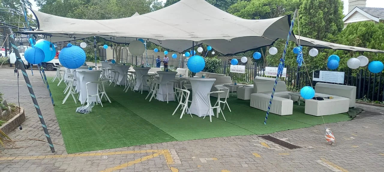 A stretch tent with blue and white lantern decorations, cocktail tables and white seating
