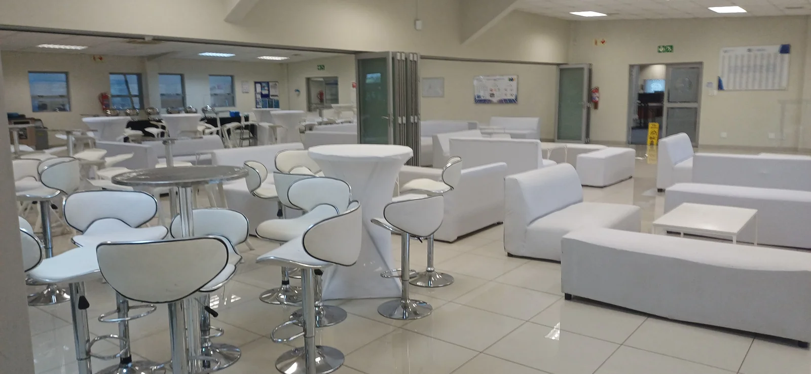 White cocktail stools and covered standing tables beside lounge sofas in an indoor venue