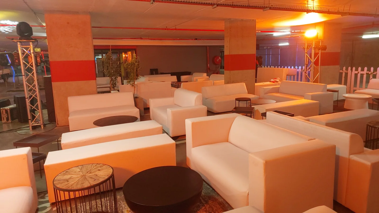 White sofas, rectangular ottomans and round low tables in a warmly lit indoor event venue