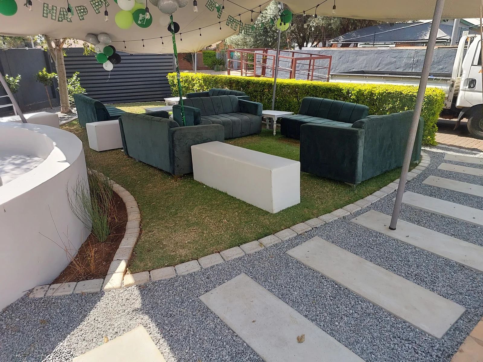 Green velvet lounge seating with white rectangular ottomans beneath a stretch tent