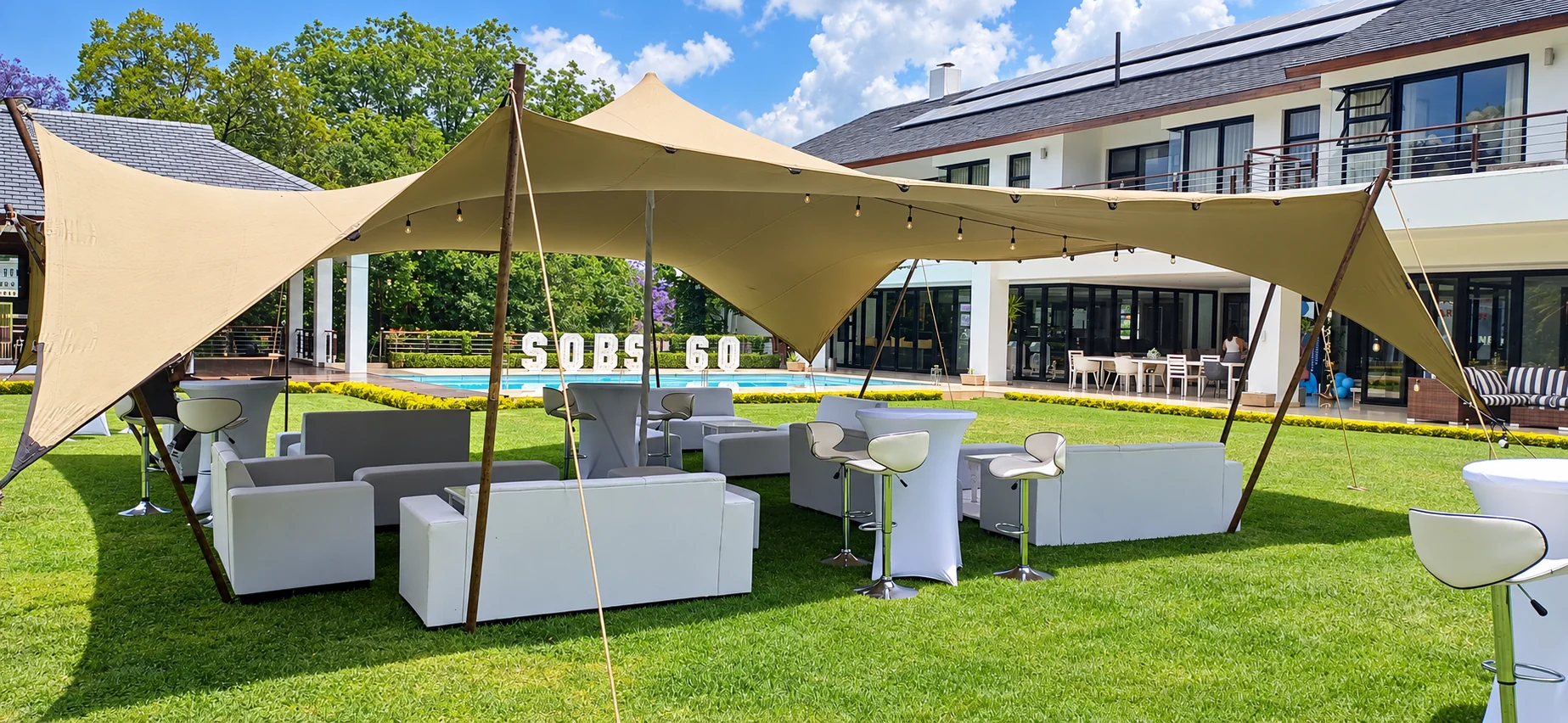 Supplied photo of white lounge sofas, cocktail tables and bar stools beneath a stretch tent on a lawn, enhanced for clarity