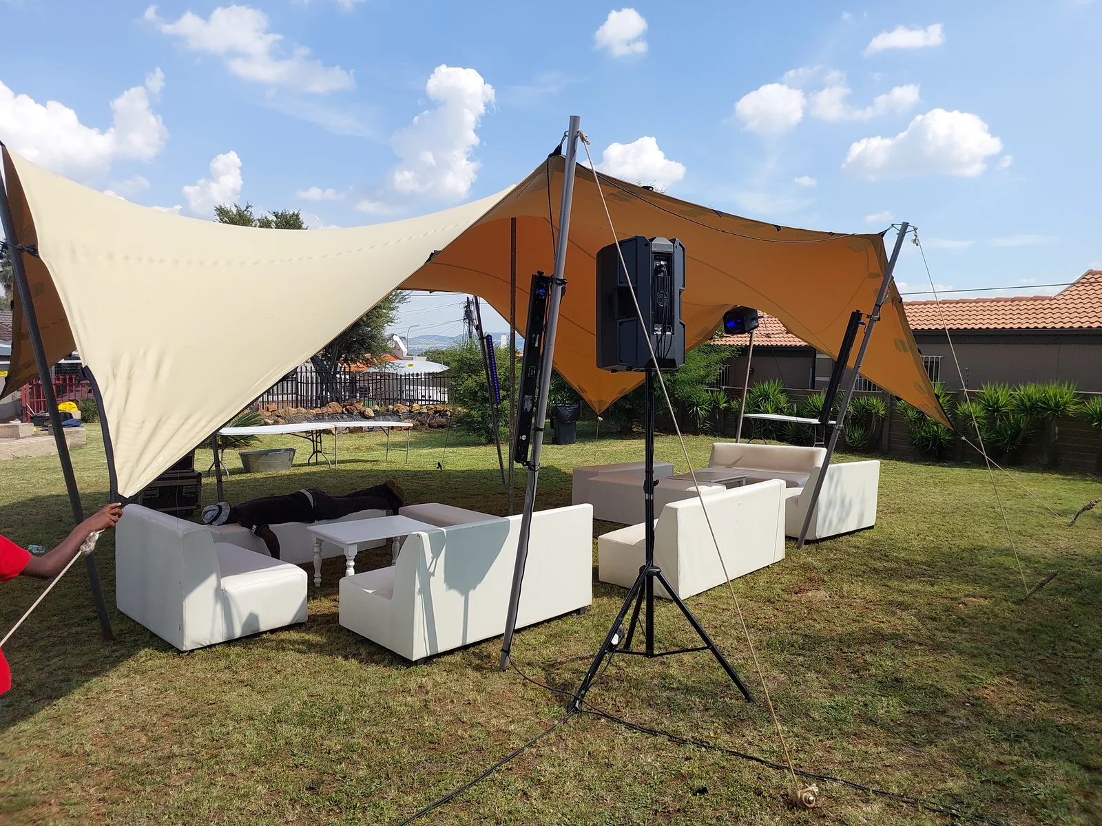 A sand-coloured stretch tent over white lounge seating and sound equipment on a lawn